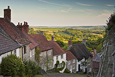 Photo of English countryside, looking down across thatched rooftops and rural land in the distance